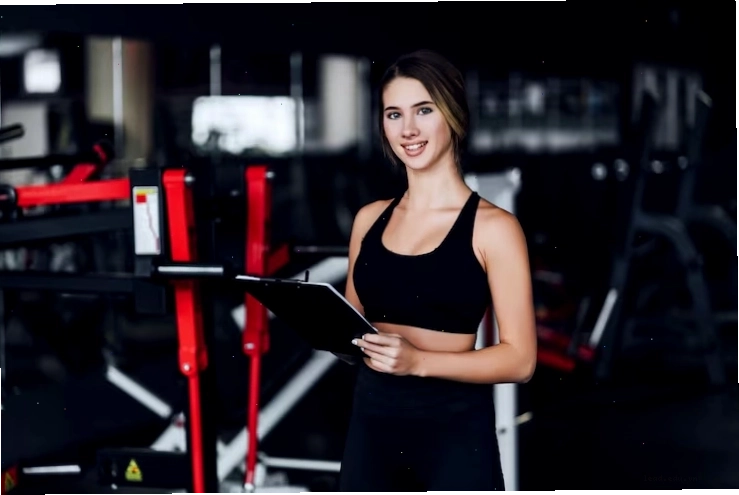 Cô gái thể thao xinh đẹp, huấn luyện viên cá nhân ở giữa phòng gym hiện đại với kế hoạch tập luyện trên tay