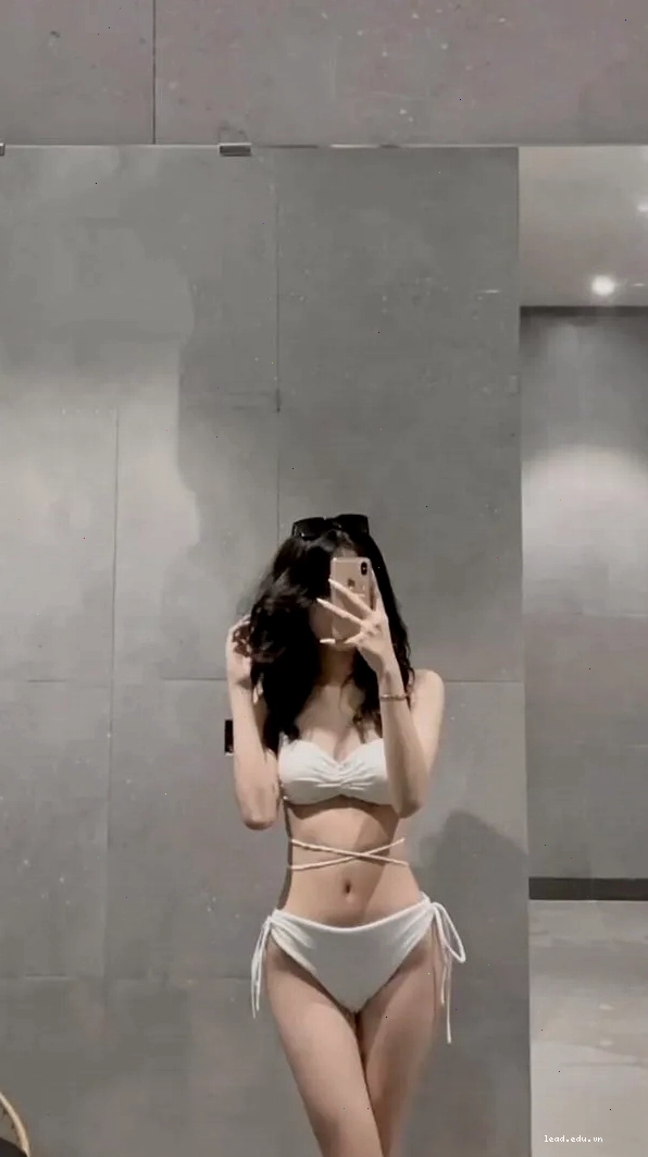 Gái đẹp trong váy body sáng màu đứng duyên dáng trước gương phòng tắm