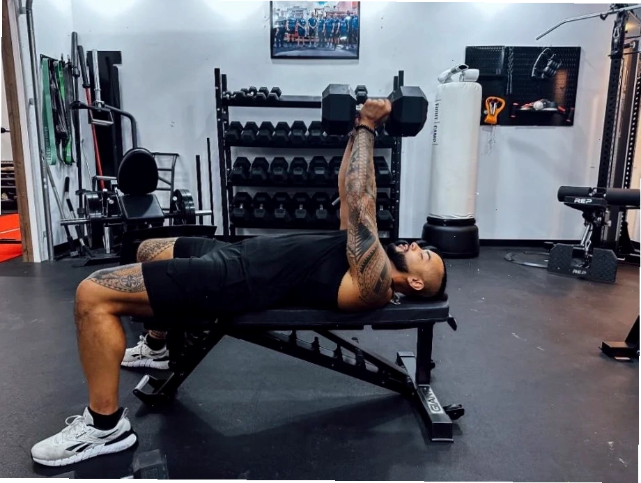 Huấn luyện viên thực hiện bài ép ngực với tạ đơn trên một chiếc gym bench điều chỉnh