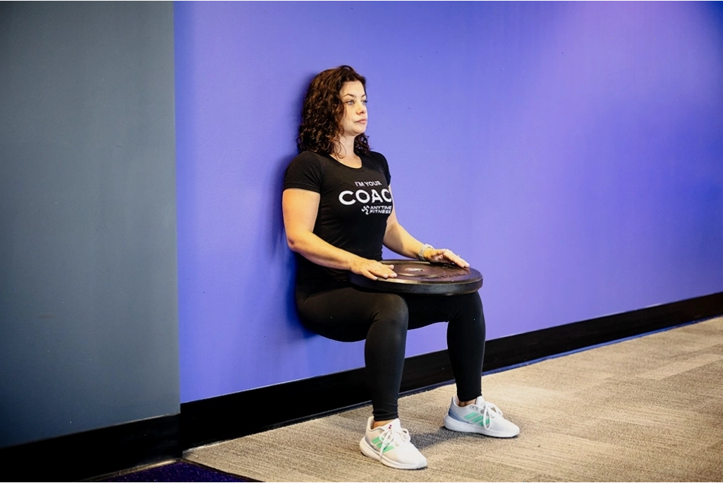 Phụ nữ thực hiện bài tập wall sit với kháng lực đĩa để tăng cường sức mạnh và sức bền phần thân dưới